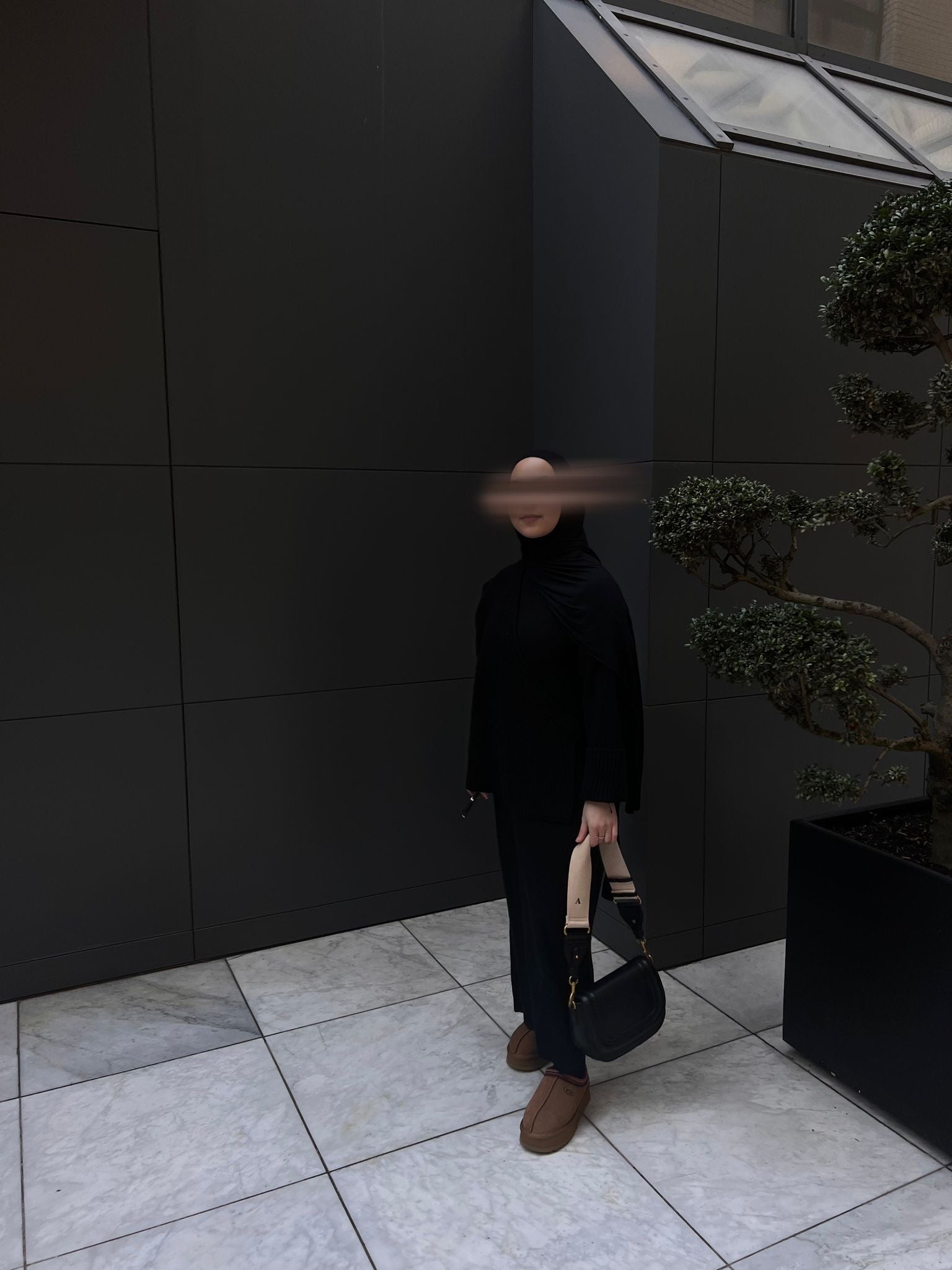 Model draagt de zwarte overslag tricot jurk van ByLiya, een elegante 2-delige jurk met een onderjurk en wikkelstuk, perfect voor een modest look.