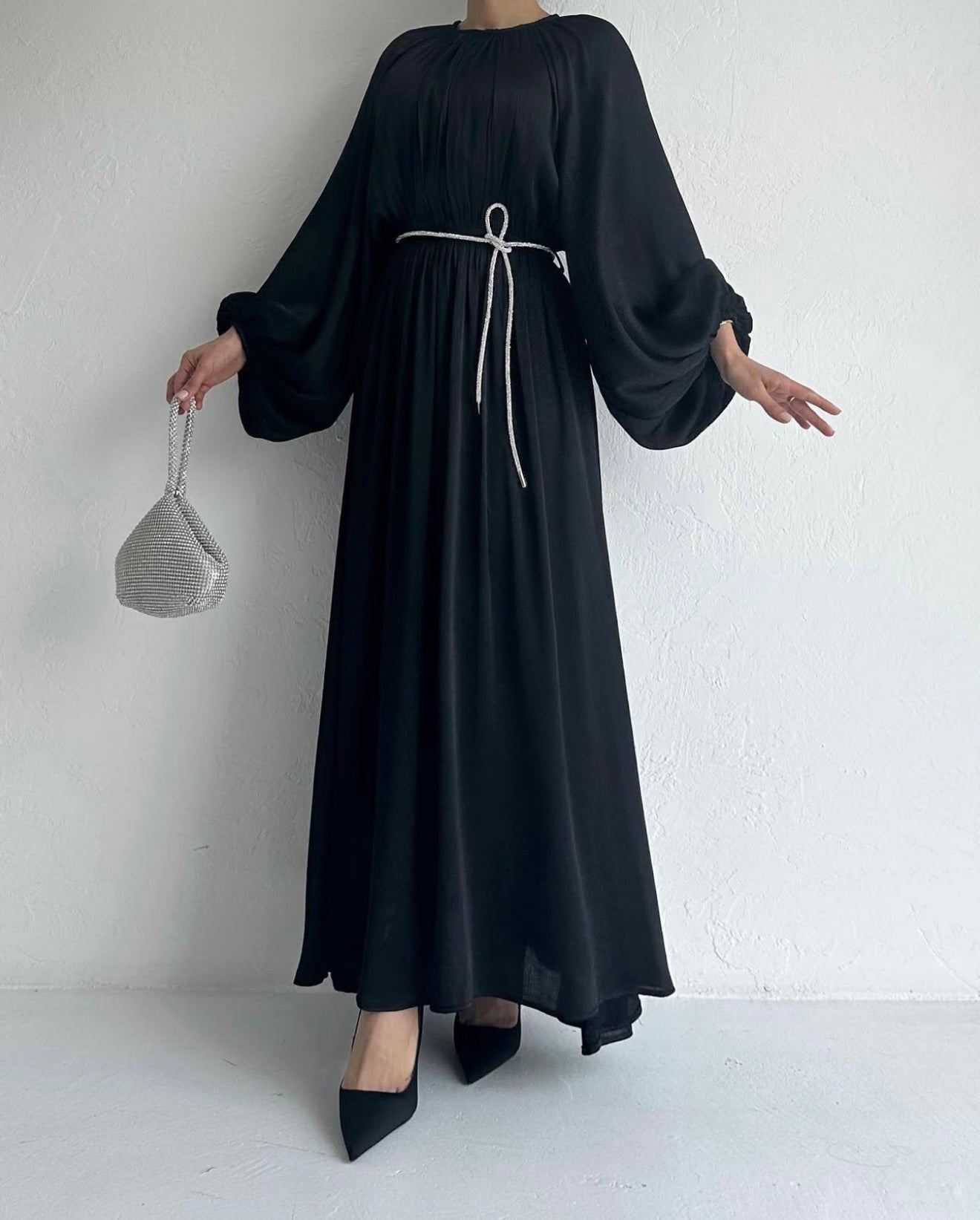 Model draagt de Laiba Dress in zwart – rechte OneSize maxi jurk met losvallende pasvorm en lange mouwen