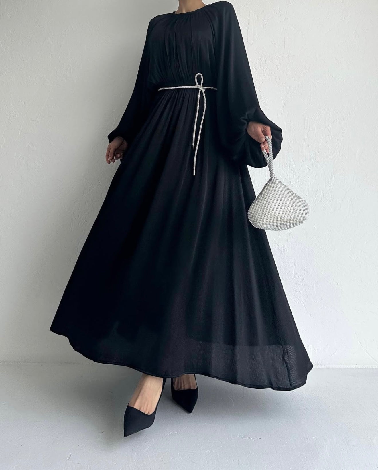 Model draagt de Laiba Dress in zwart – rechte OneSize maxi jurk met losvallende pasvorm en lange mouwen