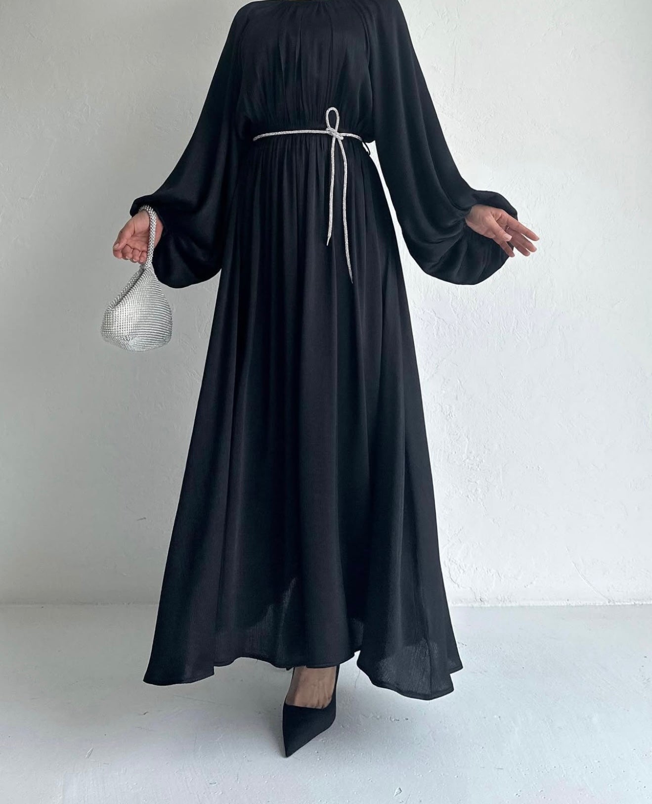 Model draagt de Laiba Dress in zwart – rechte OneSize maxi jurk met losvallende pasvorm en lange mouwen