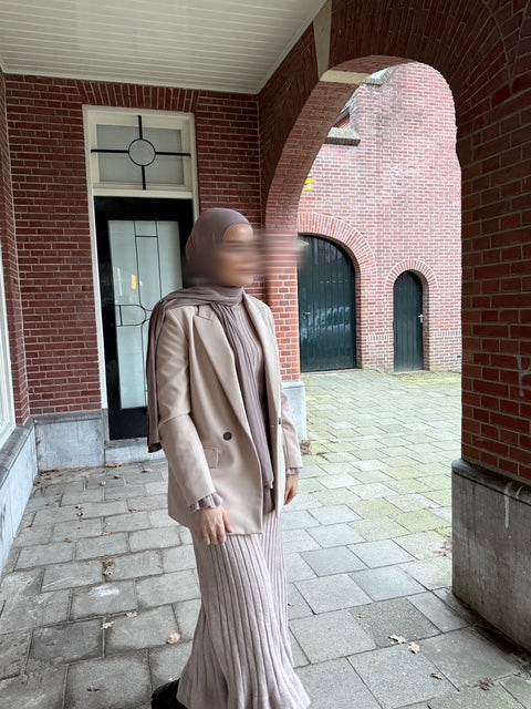 Model draagt de Lia maxi jurk van ByLiya in taupe, gestyled met een blazer voor een modest en elegante look.