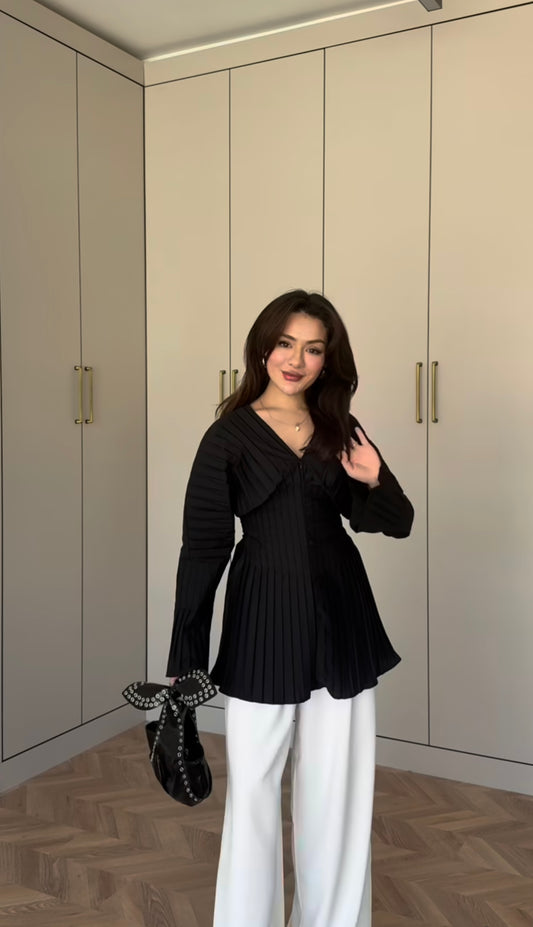 Modest fashion ook met een elegante zwarte geplooide blouse, lange mouwen en een v-hals. Gedragen op een witte pantalon.