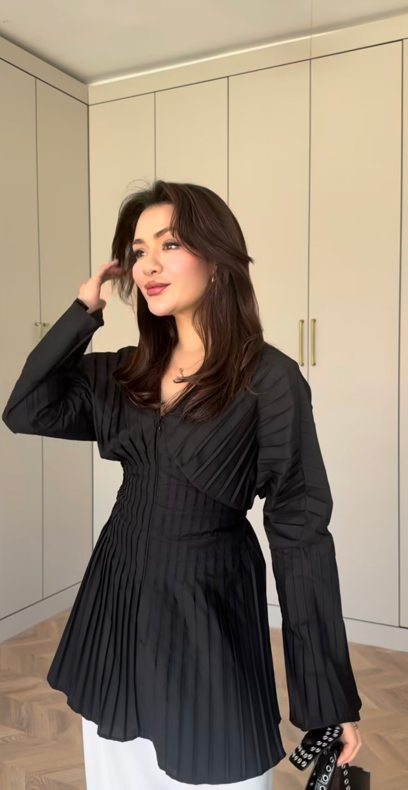 Modest fashion ook met een elegante zwarte geplooide blouse, lange mouwen en een v-hals. Gedragen op een witte pantalon.