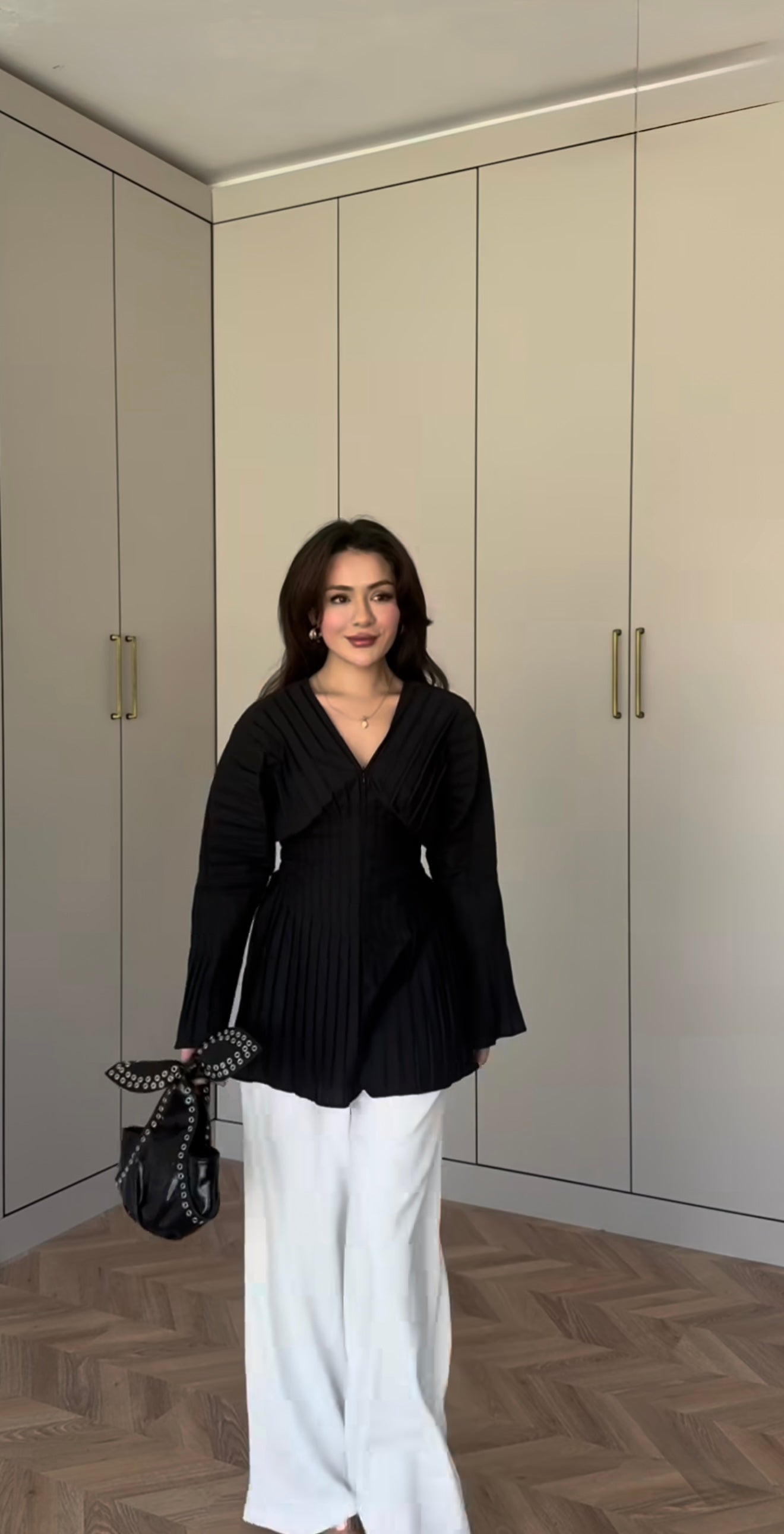 Modest fashion ook met een elegante zwarte geplooide blouse, lange mouwen en een v-hals. Gedragen op een witte pantalon.