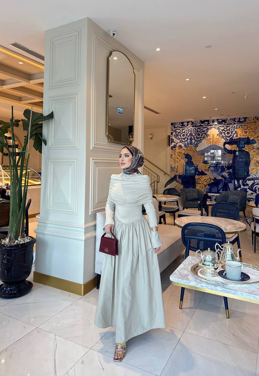 Elegante beige maxi-jurk met drape details aan de voorzijde, lange mouwen en een flatterende pasvorm – ideaal voor een stijlvolle, bescheiden look