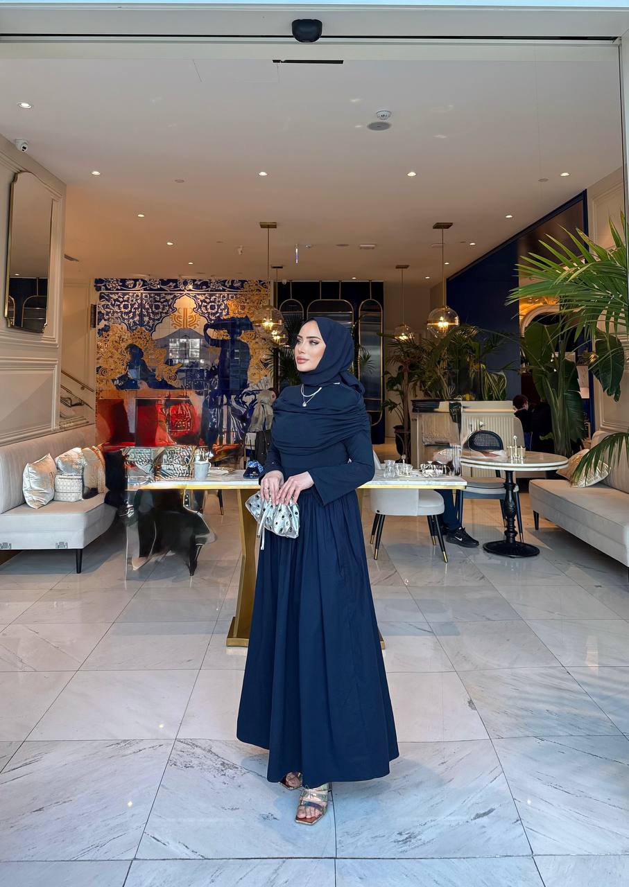 Elegante marine-blauw maxi-jurk met drape details aan de voorzijde, lange mouwen en een flatterende pasvorm – ideaal voor een stijlvolle, bescheiden look