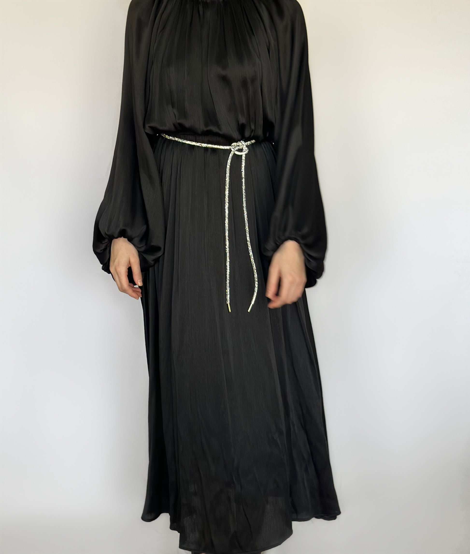 Laiba maxi jurk van ByLiya, zwarte losvallende jurk met lange mouwen, subtiele plooien en een bijpassende ceintuur versierd met steentjes voor een elegante touch.