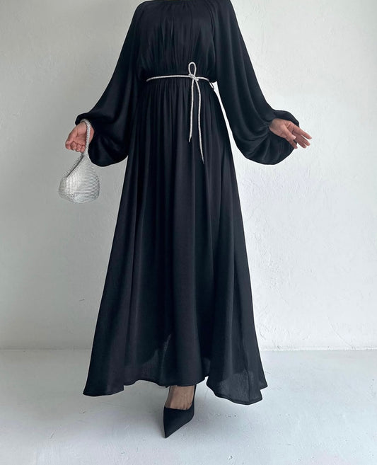 Model draagt de Laiba Dress in zwart – rechte OneSize maxi jurk met losvallende pasvorm en lange mouwen