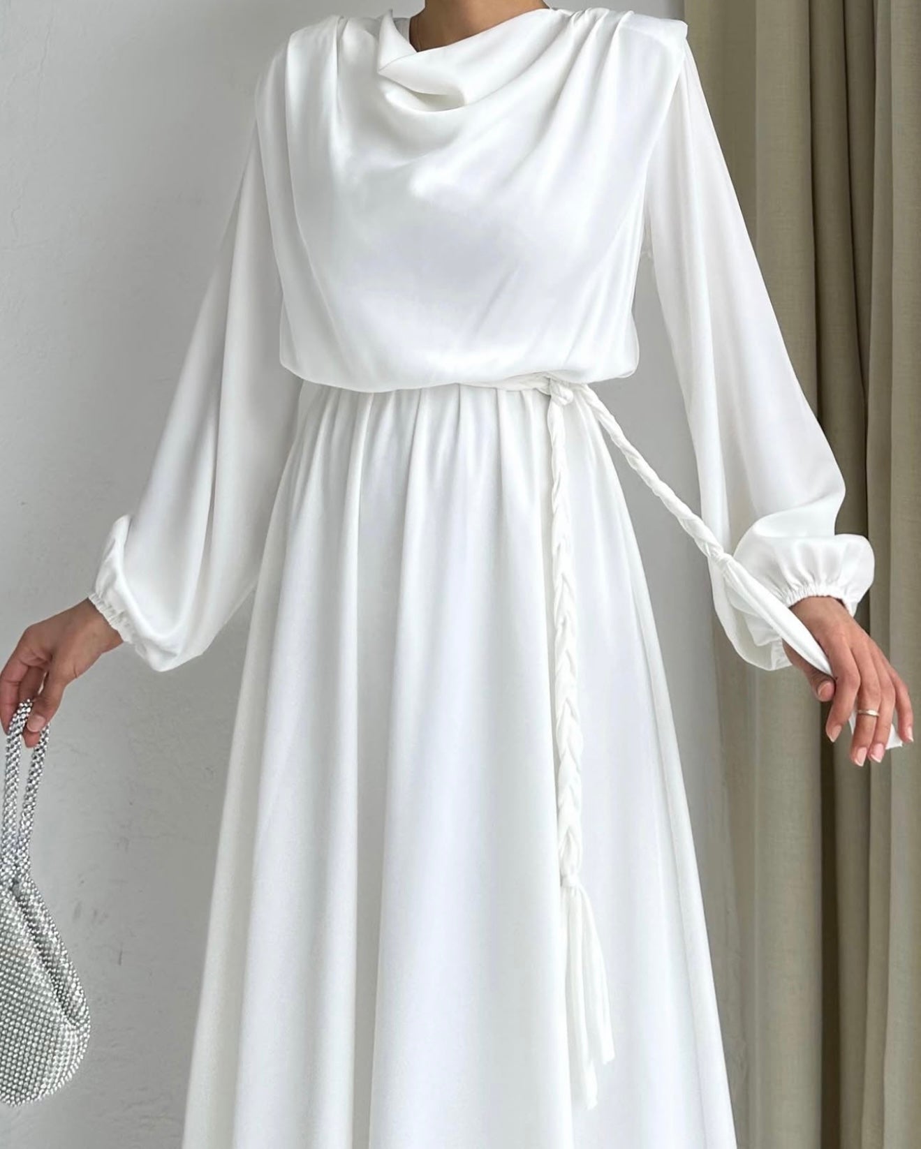 Model draagt de Liyana Dress in wit – losvallende maxi jurk met rechte snit en strikceintuur in de taille