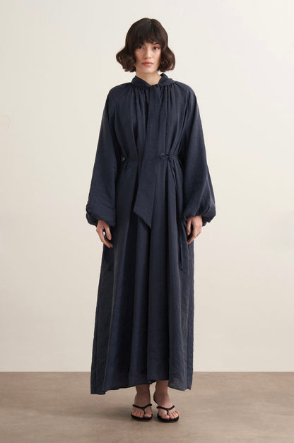 Maira maxi-jurk voor dames in marineblauw met verstelbaar taillelint, lange pofmouwen, hoge halslijn en soepelvallende stof, elegant modest fashion model.