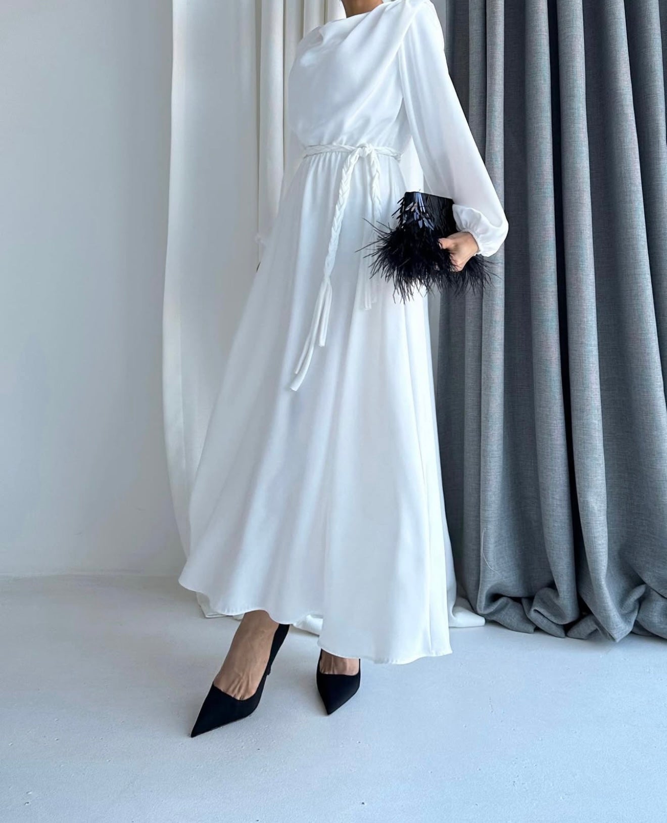 Model draagt de Liyana Dress in wit
 – losvallende maxi jurk met rechte snit en strikceintuur in de taille