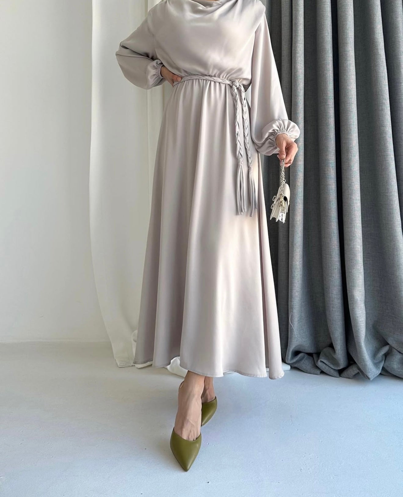 Model draagt de Liyana Dress in beige – losvallende maxi jurk met rechte snit en strikceintuur in de taille