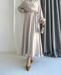 Model draagt de Liyana Dress in beige – losvallende maxi jurk met rechte snit en strikceintuur in de taille