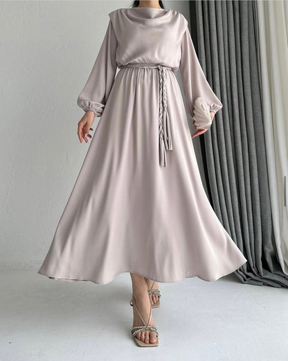 Model draagt de Liyana Dress in beige – losvallende maxi jurk met rechte snit en strikceintuur in de taille