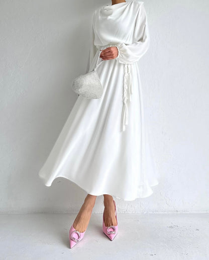 Model draagt de Liyana Dress in wit – losvallende maxi jurk met rechte snit en strikceintuur in de taille