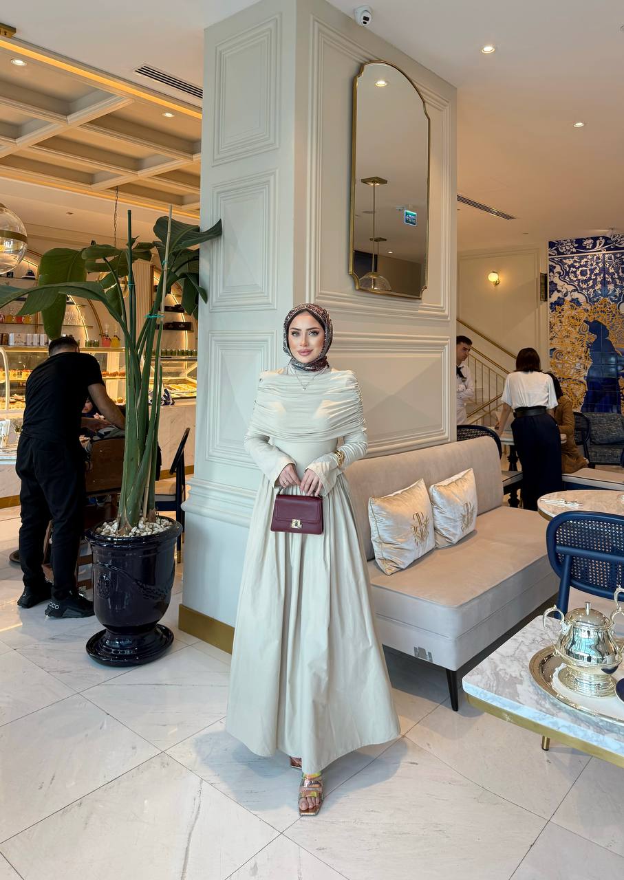 Elegante beige maxi-jurk met drape details aan de voorzijde, lange mouwen en een flatterende pasvorm – ideaal voor een stijlvolle, bescheiden look