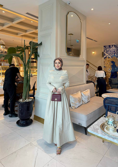 Elegante beige maxi-jurk met drape details aan de voorzijde, lange mouwen en een flatterende pasvorm – ideaal voor een stijlvolle, bescheiden look