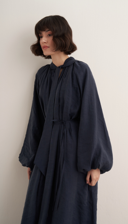 Maira maxi-jurk voor dames in marineblauw met verstelbaar taillelint, lange pofmouwen, hoge halslijn en soepelvallende stof, elegant modest fashion model.